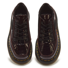 Load image into Gallery viewer, A pair of Dr. Martens low-top lace-up boots in glossy dark burgundy crocodile-embossed patent leather, featuring black laces and signature yellow stitching around the sole edge, shown against a plain white background.