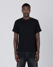 Load image into Gallery viewer, A man wearing a black short-sleeve ribbed knit t-shirt and dark gray jeans, standing against a light gray studio background.