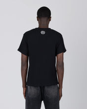 Load image into Gallery viewer, A man viewed from behind wearing a black ribbed short-sleeve t-shirt with a small circular logo on the upper back, paired with dark gray jeans, against a light gray studio background.