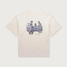 Load image into Gallery viewer, A cream-colored short-sleeve t-shirt featuring a vintage-style graphic print of a family in a car on the front, with a small signature detail below, displayed flat against a light off-white background.