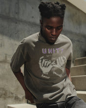 Load image into Gallery viewer, A man wearing a gray graphic t-shirt with purple and white text reading 'UNITY Since Aenor' and a hand graphic, posing on concrete stairs.